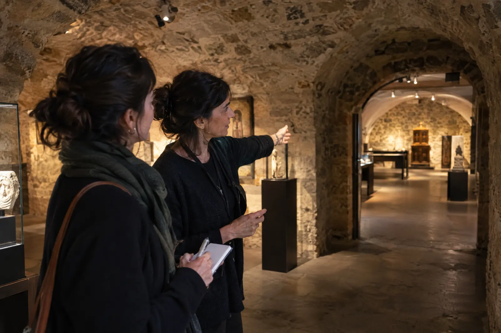 Dans des caves voûtées, la personne responsable explique le parcours de visite à un nouveau guide